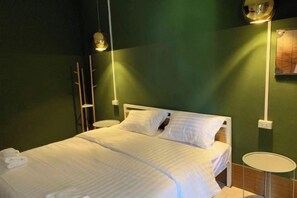 A bed with white linens, a bedside table, and a wall-mounted lamp. - You empire Hostel and Bar (Pakse)