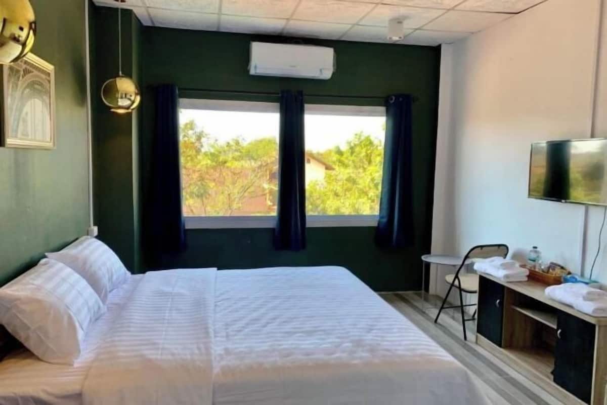 A hotel room with a bed, a desk with a chair, a TV, and a window with curtains.