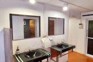 A bathroom with two sinks, a mirror, a towel dispenser, and a shower. - You empire Hostel and Bar (Pakse)