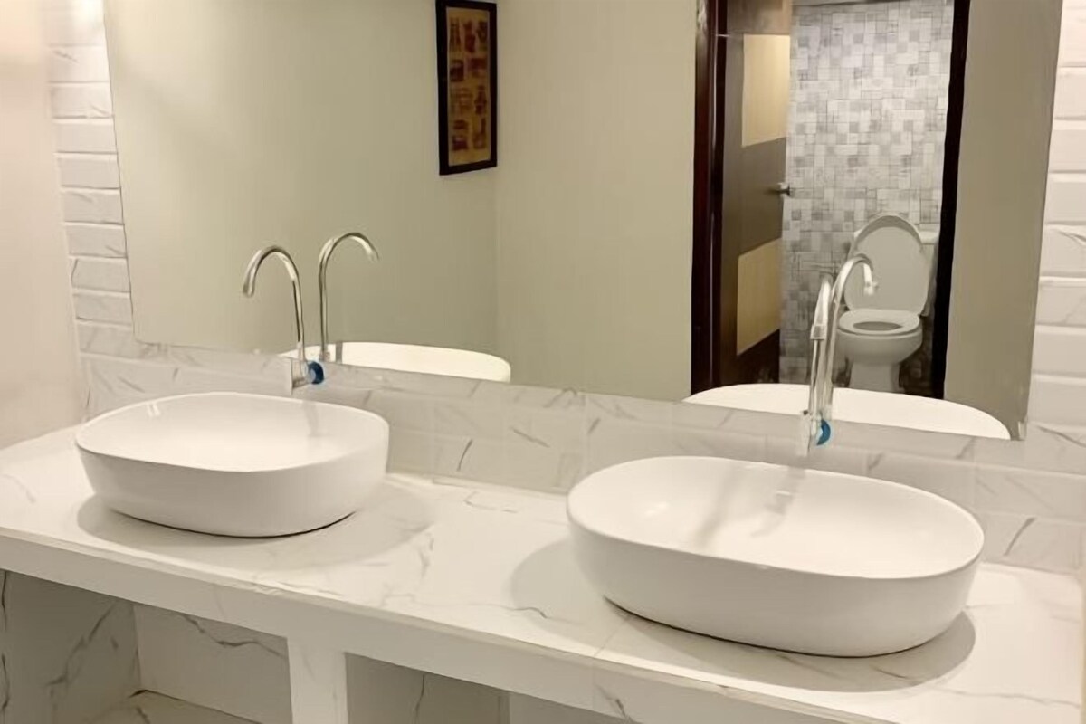 A bathroom with two white vessel sinks, a mirror, and a framed picture on the wall.