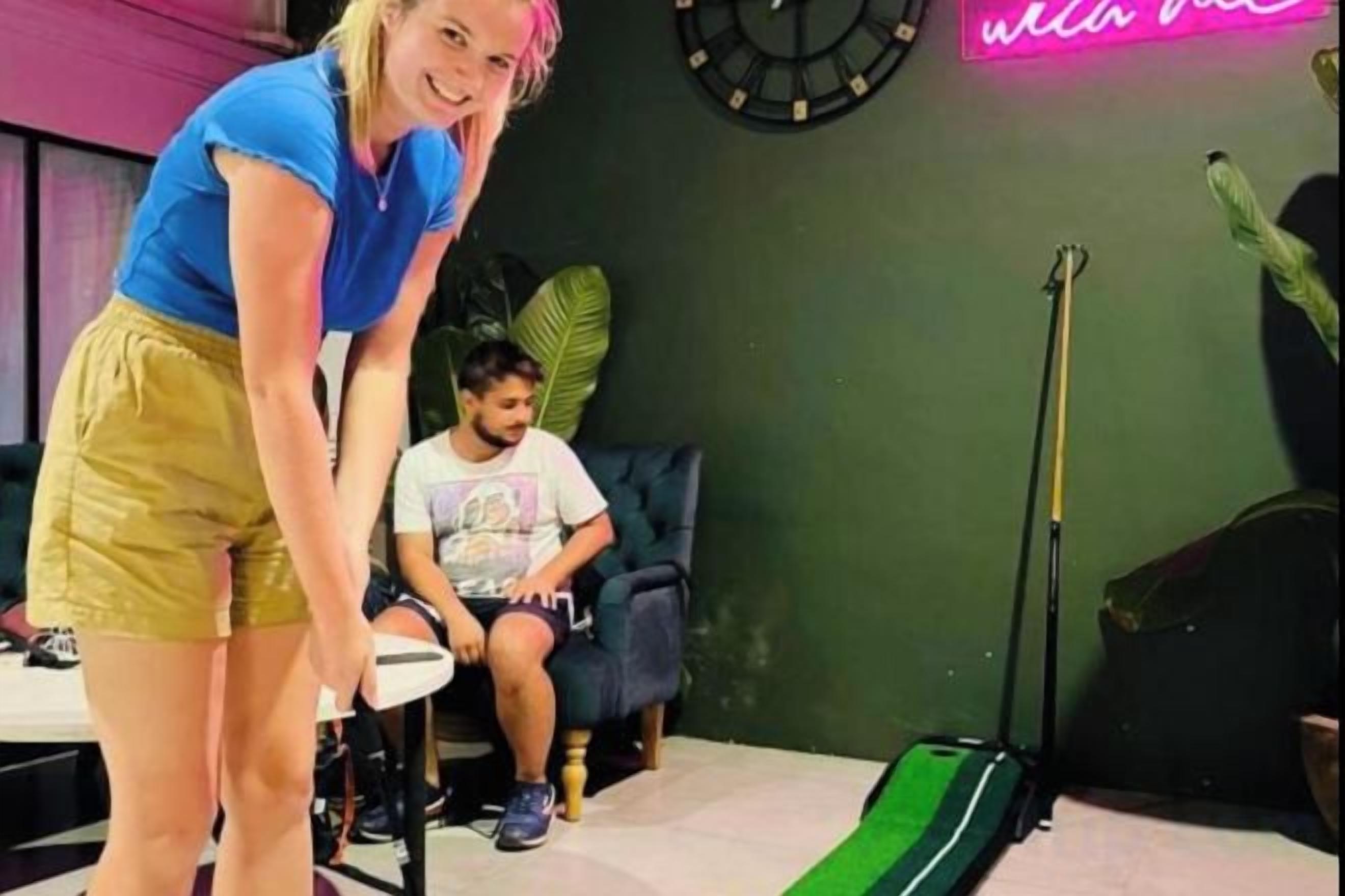 A room with a green floor, a clock on the wall, and a neon sign.