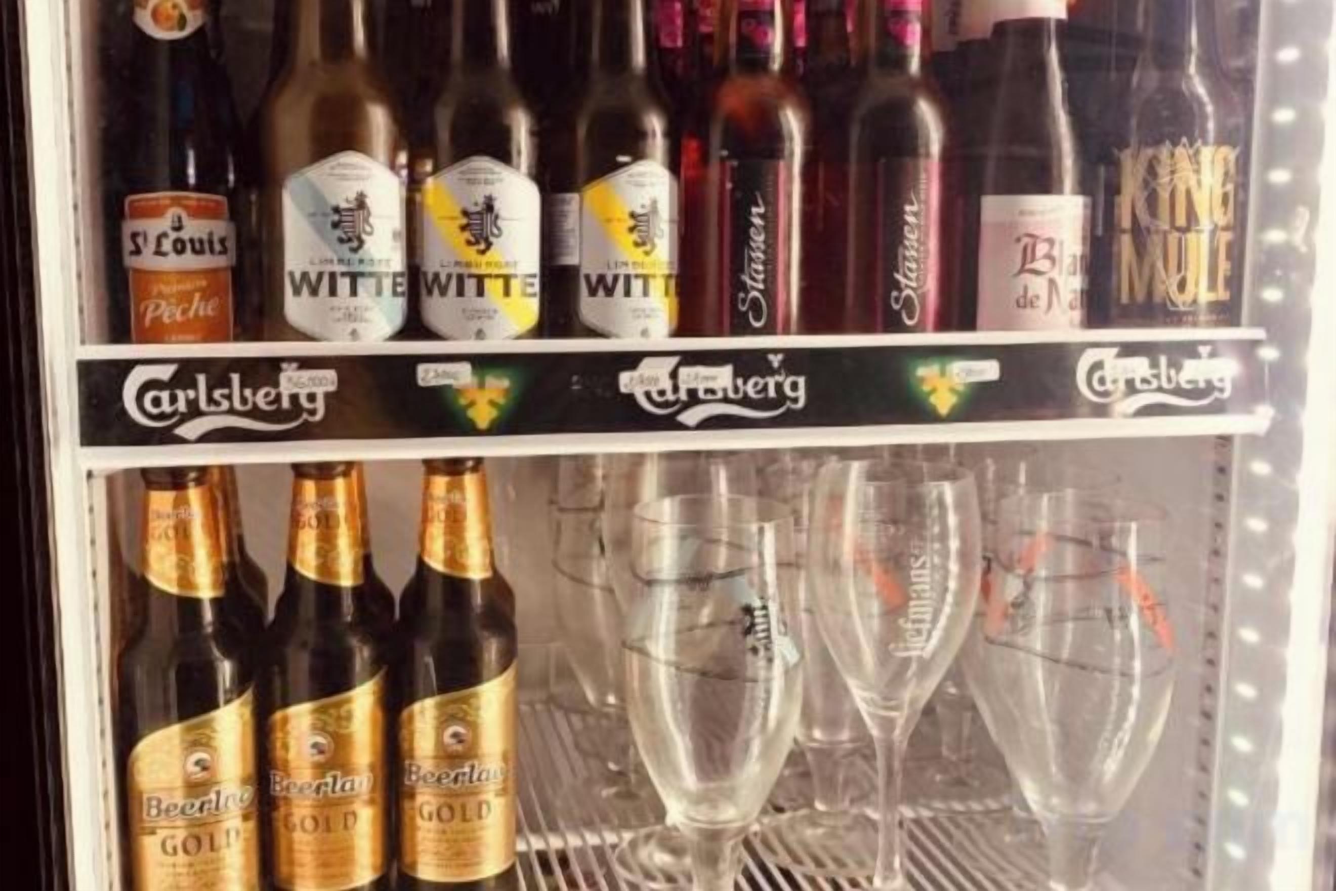 Ein gekühlter Kühlregal mit verschiedenen Bier- und Weinflaschen sowie leeren Weingläsern.