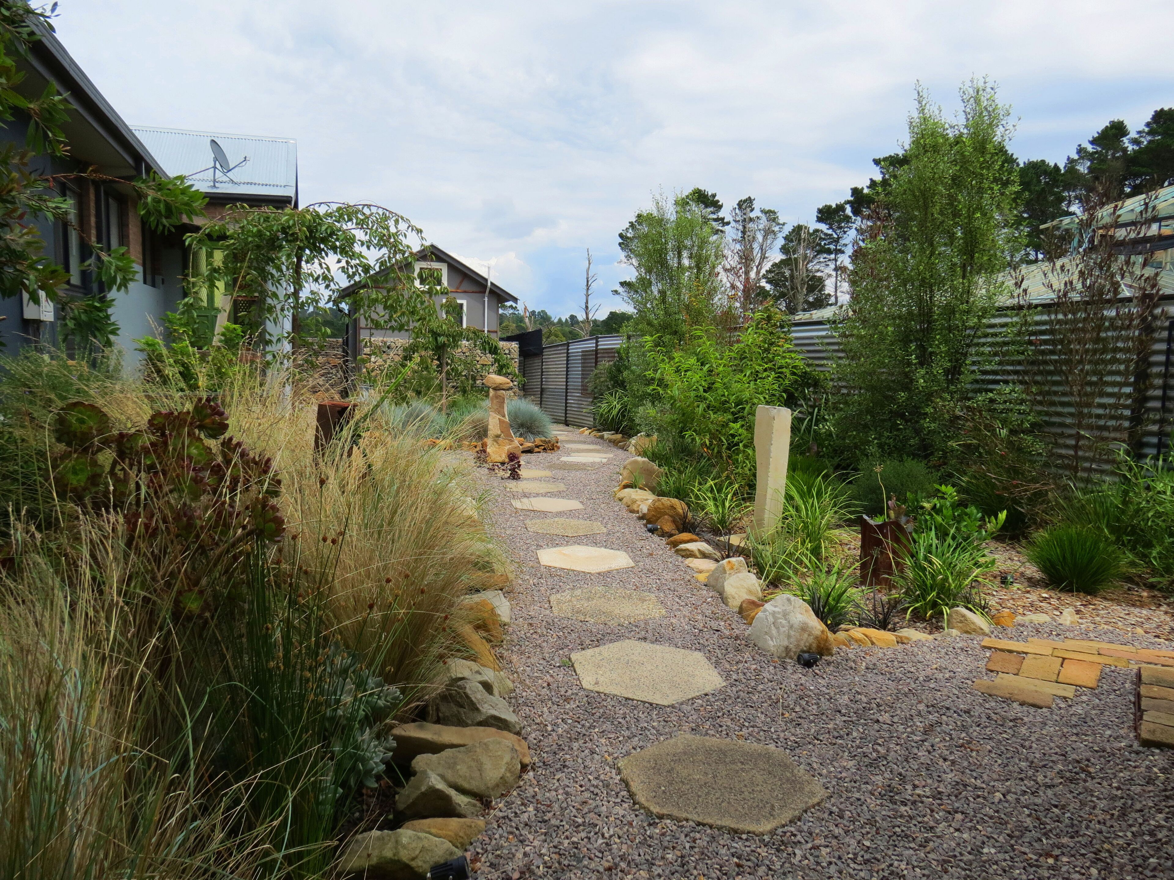 Un sentier de jardin bordé de pierres plates servant de marchepied, entouré de différentes plantes et d’une clôture.