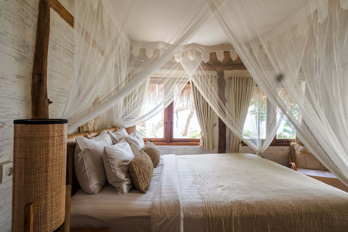 Un dormitorio con cama con dosel, vigas de madera y una cesta de mimbre junto a la cama.