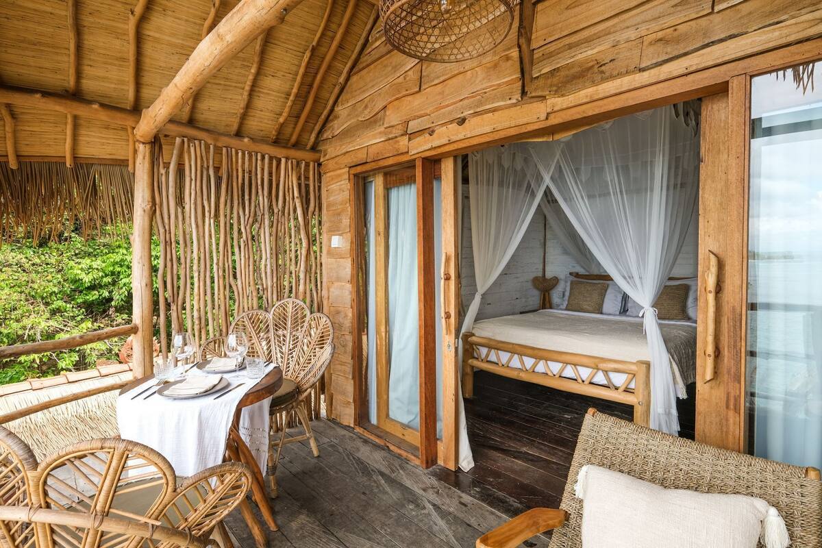 Una cabaña de madera con comedor, una cama con dosel y vistas al verdor.
