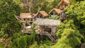A cluster of thatched-roof cottages nestled in a lush forest, connected by wooden walkways. - The Korowai (Pecatu)