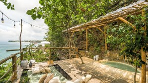 A wooden deck with a hot tub, lounge chairs, and a pergola overlooking a body of water. - The Korowai (Pecatu)