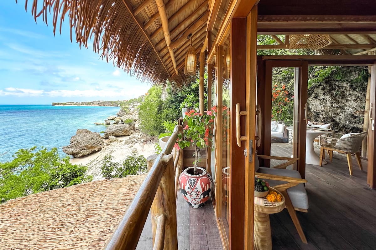 Terraza de madera con muebles de mimbre con vistas a una playa y al mar.