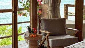 A wooden deck with a cushioned chair and a table with a fruit bowl. - The Korowai (Pecatu)