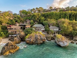 A coastal property with multiple buildings, including a large house with a balcony, situated on a cliff overlooking the sea.