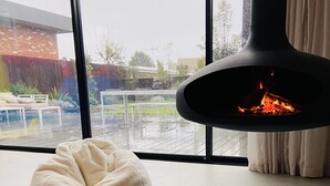 A cozy room with a large window, a white bean bag chair, a blue patterned rug, and a black fireplace. - LUXE poolside living, in the heart of Flinders. (Flinders)