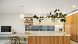 A modern kitchen with a central island, wooden cabinets, and hanging plants. - LUXE poolside living, in the heart of Flinders. (Flinders)