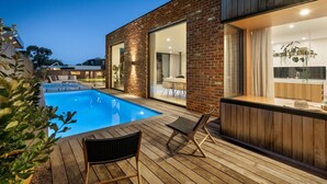 A modern house with a swimming pool, wooden deck, and a kitchen with large windows. - LUXE poolside living, in the heart of Flinders. (Flinders)