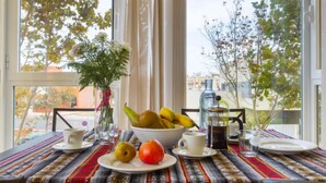 A dining table with a fruit bowl, cups, and a coffee pot, set against a window with a view of trees and buildings. - Carnaval by Interhome (Isla Cristina)
