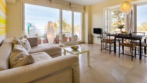 A living room with a sofa, a dining table with chairs, a TV, and large windows with curtains. - Carnaval by Interhome (Isla Cristina)
