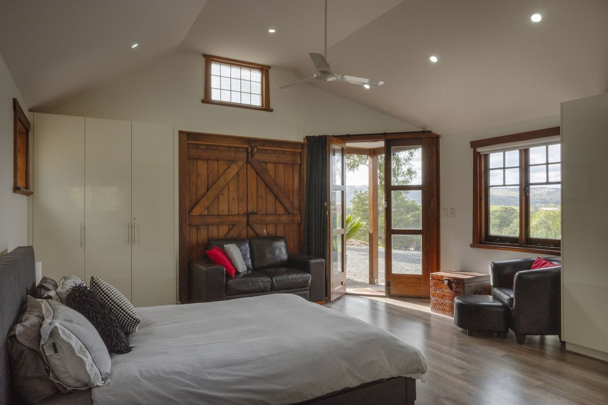 A bedroom with a large bed, a wooden wardrobe, a sofa, and a view through the door.