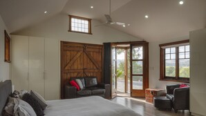 A bedroom with a large bed, a wooden wardrobe, a sofa, and a view through the door. - 131 Your Vineyard Home in the heart of the Vale (McLaren Flat)