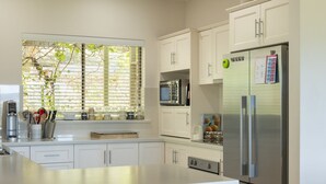 A modern kitchen with white cabinetry, a large island with stools, stainless steel appliances, and a window with blinds. - 131 Your Vineyard Home in the heart of the Vale (McLaren Flat)