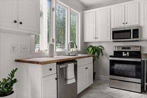 A modern kitchen with white cabinetry, a wooden countertop, a stainless steel sink, a microwave, and an oven.