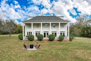 A large, two-story house with a front porch, surrounded by a well-maintained lawn and trimmed bushes.
