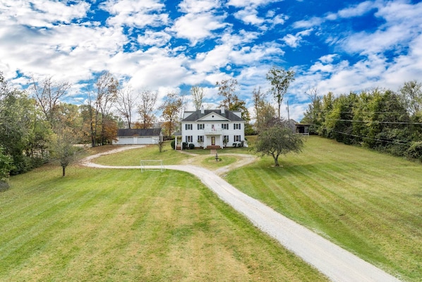 A large, two-story house with a well-maintained lawn and a gravel driveway leading to the front door.