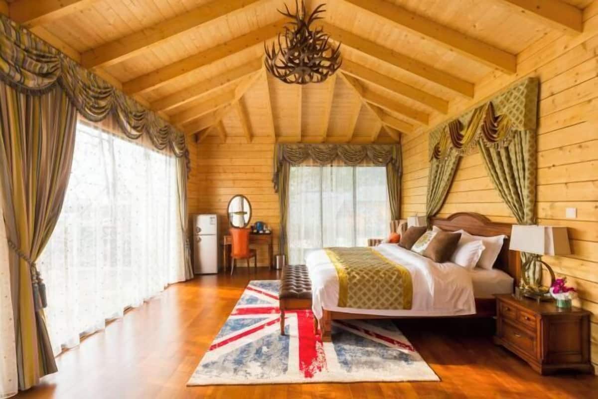 Un dormitorio de cabaña de madera con cama, mesita de noche, lámpara y escritorio con silla.