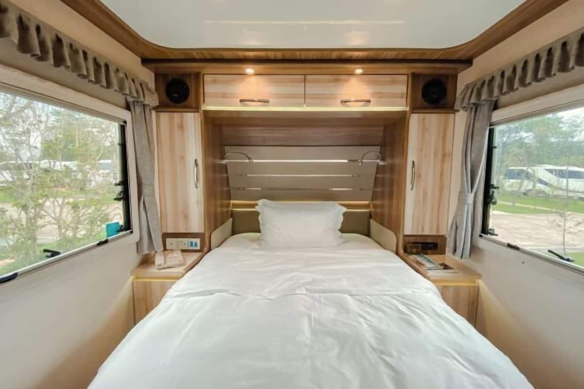 Un dormitorio con cama, mesitas de noche, cabecero y ventanas.