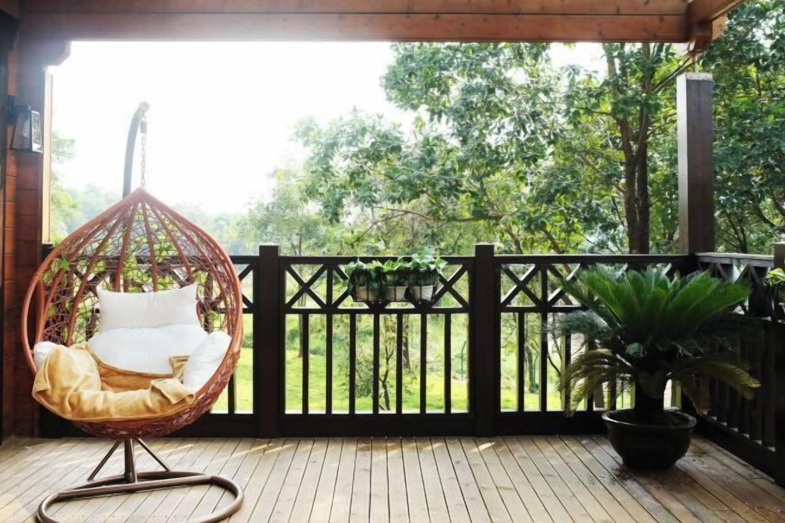 Une terrasse en bois avec un fauteuil suspendu et une plante en pot.