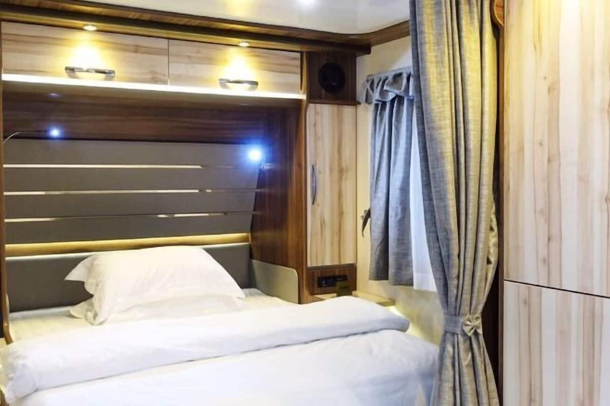 Una cama bien hecha con sábanas blancas, un cabecero de madera y una mesita de noche con una lámpara.
