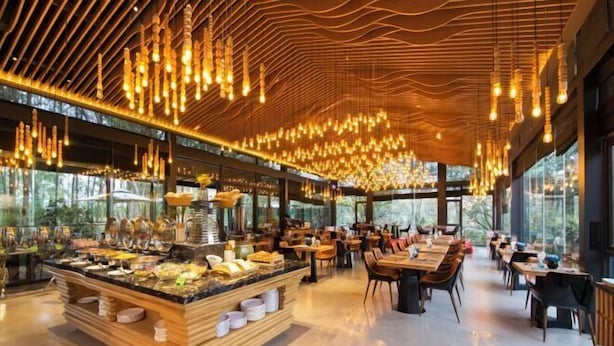 Een modern restaurant met een centraal buffet, houten plafond en grote ramen.