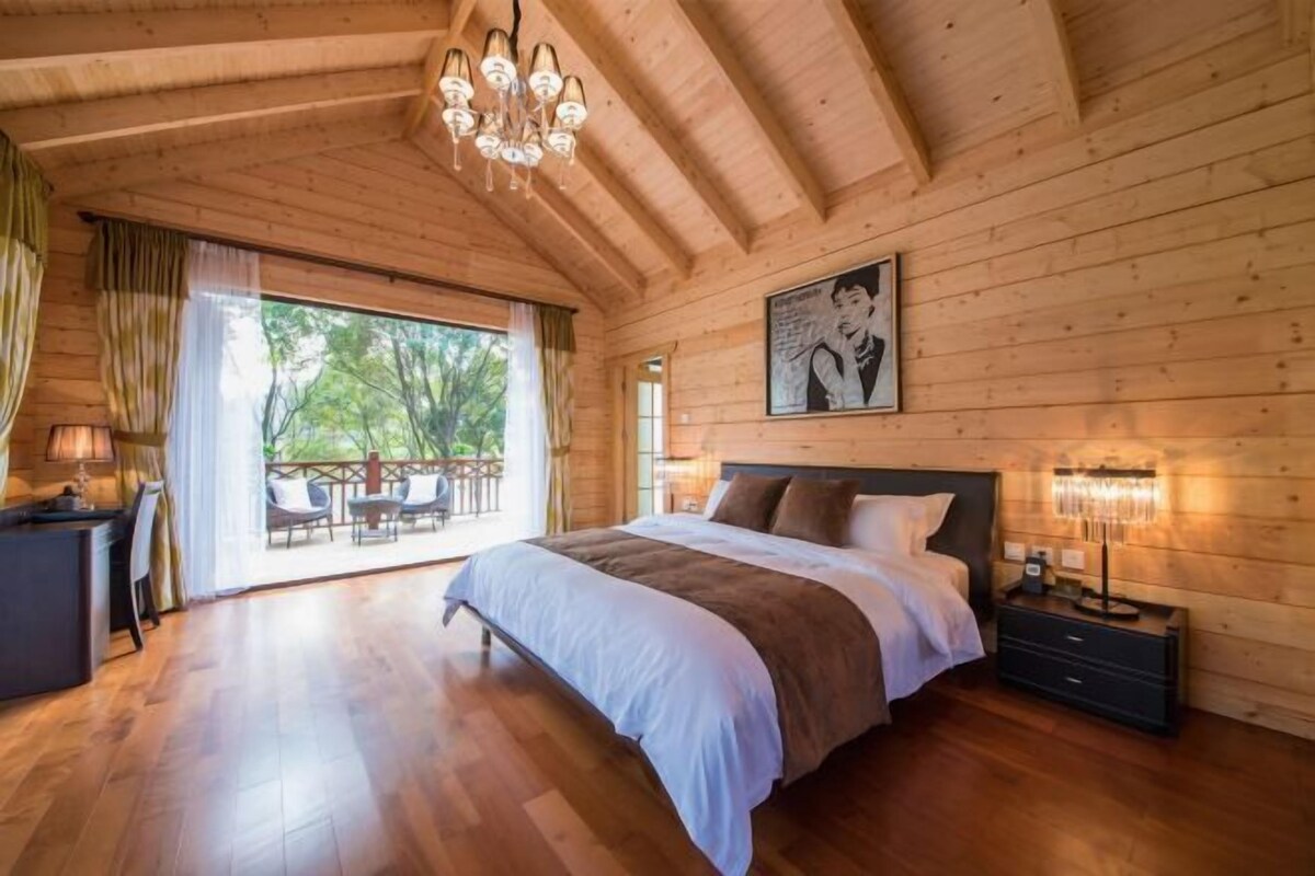 A wooden cabin bedroom with a large bed, a desk, and a balcony with outdoor furniture.