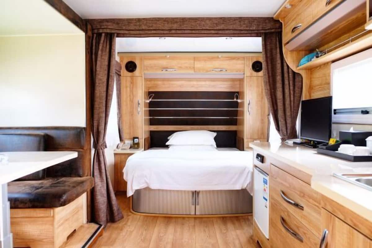Un dormitorio compacto en una caravana, con cama, una mesita pequeña, televisor integrado y un armario de almacenamiento.