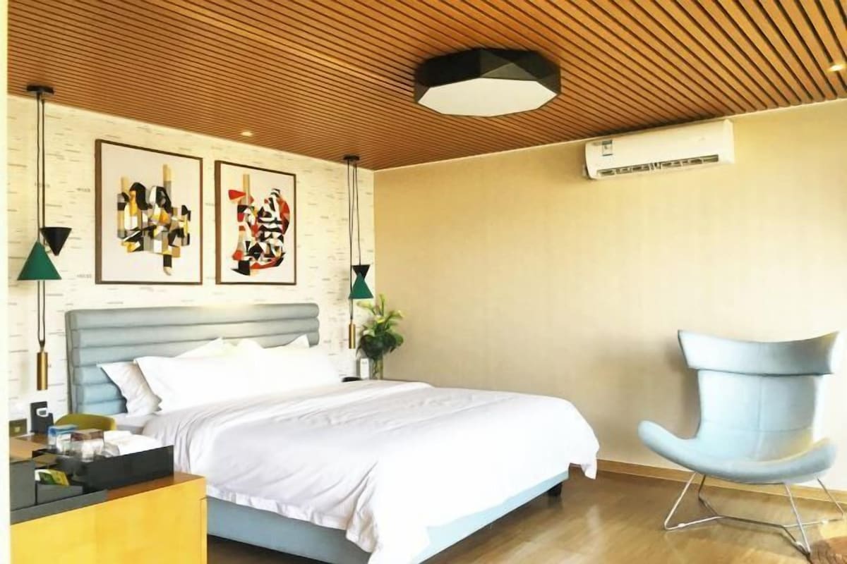 A modern bedroom with a bed, a chair, and artwork on the wall.