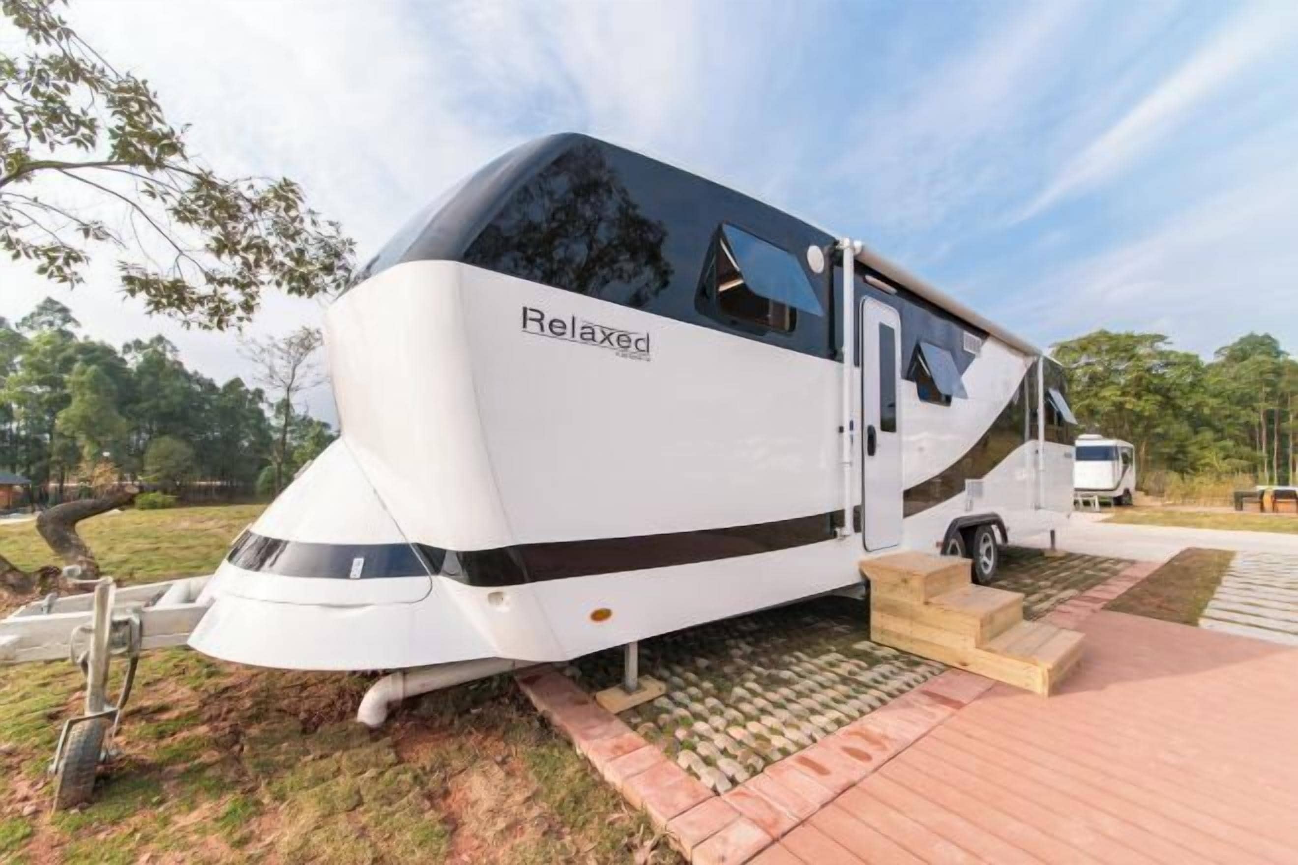 A white RV with the word "Relaxed" on its side, parked on a paved area with steps leading up to it.