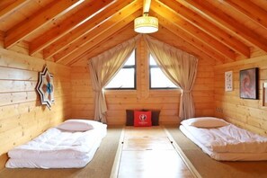 A cozy cabin with two single beds, a wooden ceiling, and a large window with curtains.