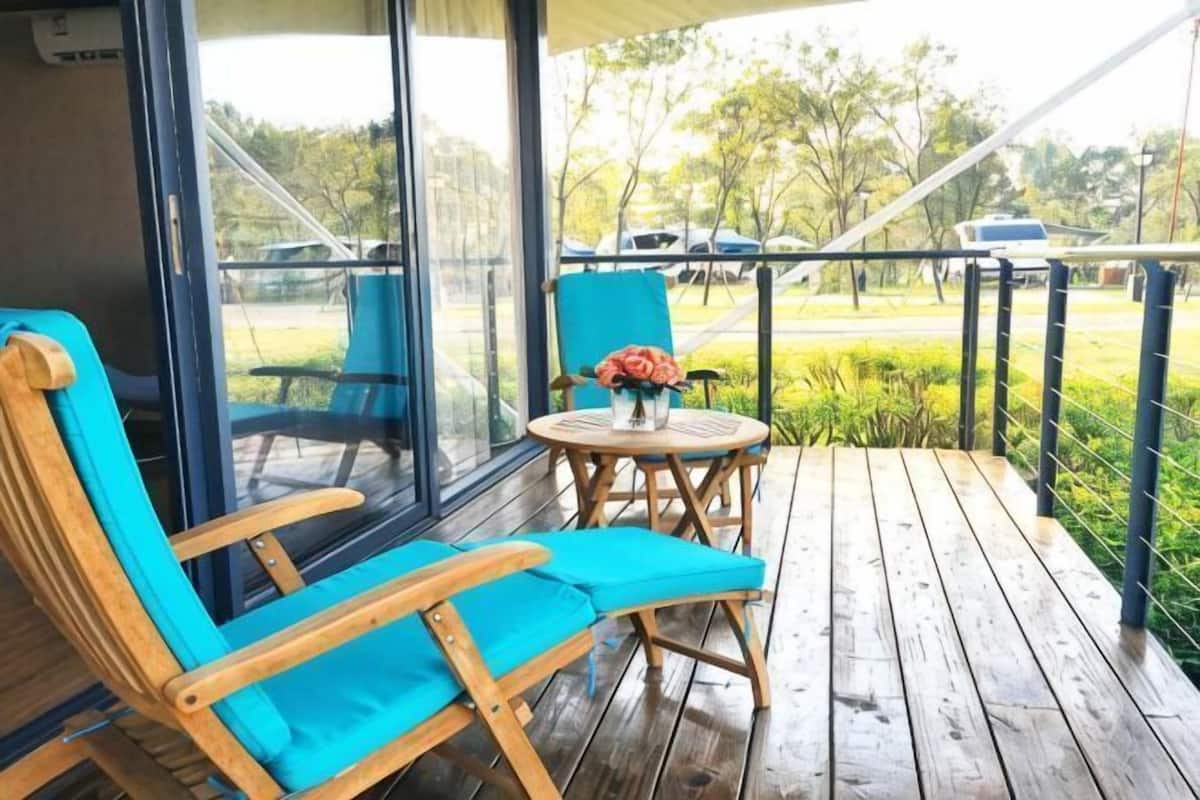 Una terraza de madera con una silla azul y una pequeña mesa con flores.