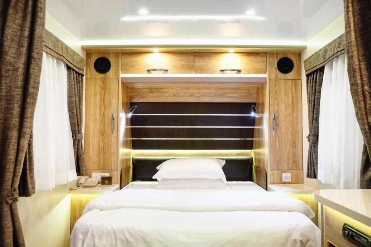 A modern bedroom with a large bed, wooden headboard, built-in shelves, and a bedside table with a lamp.