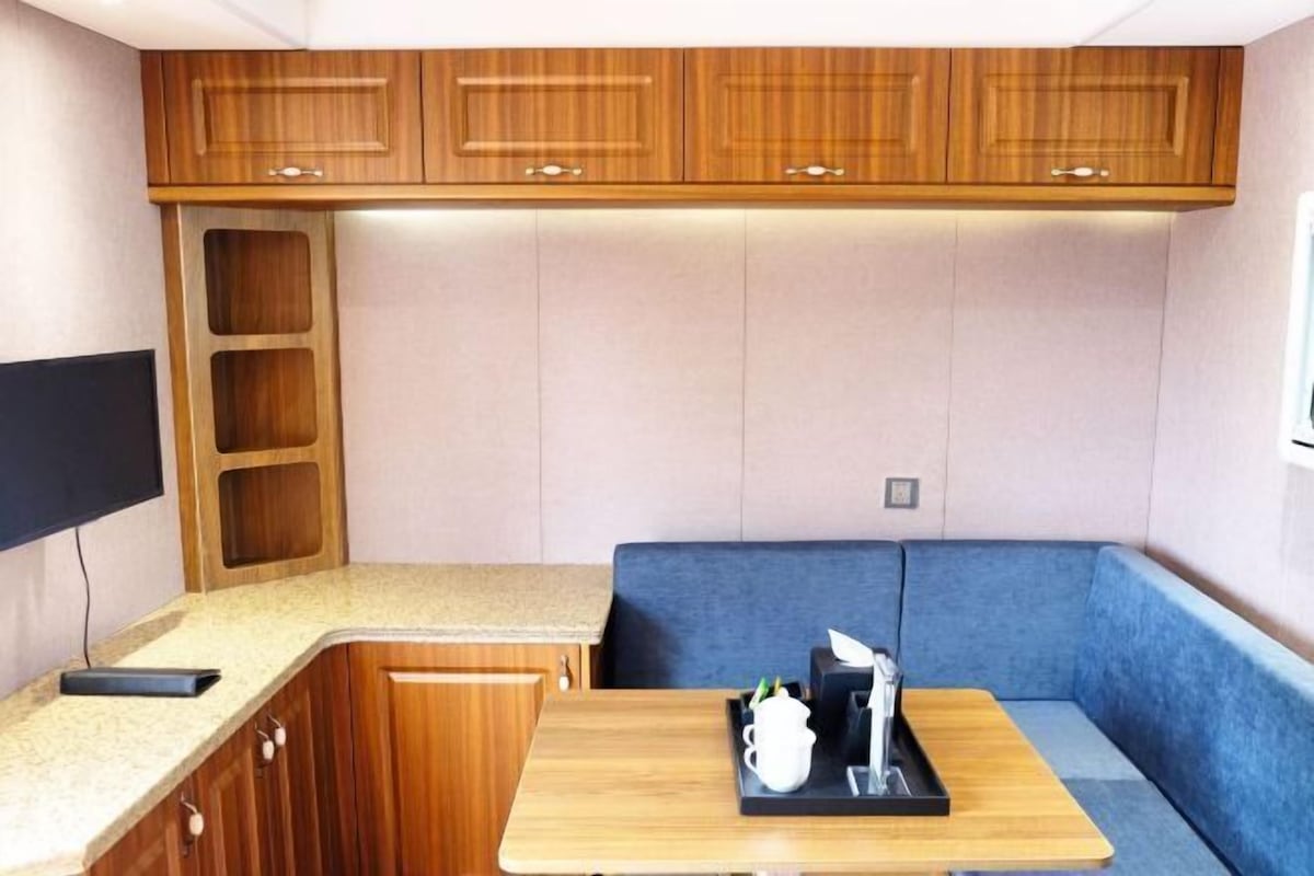 A compact kitchenette with wooden cabinets, a countertop, and a blue cushioned seating area.