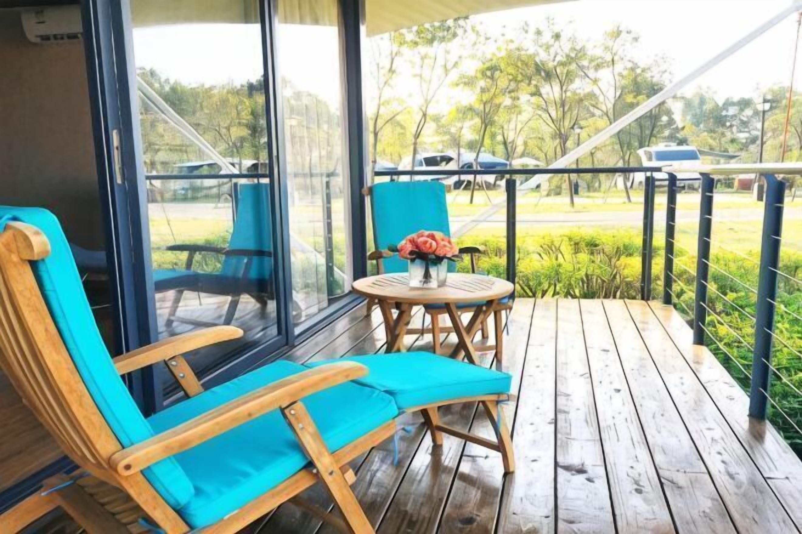 A wooden deck with a blue chair and a small table with a vase of flowers.