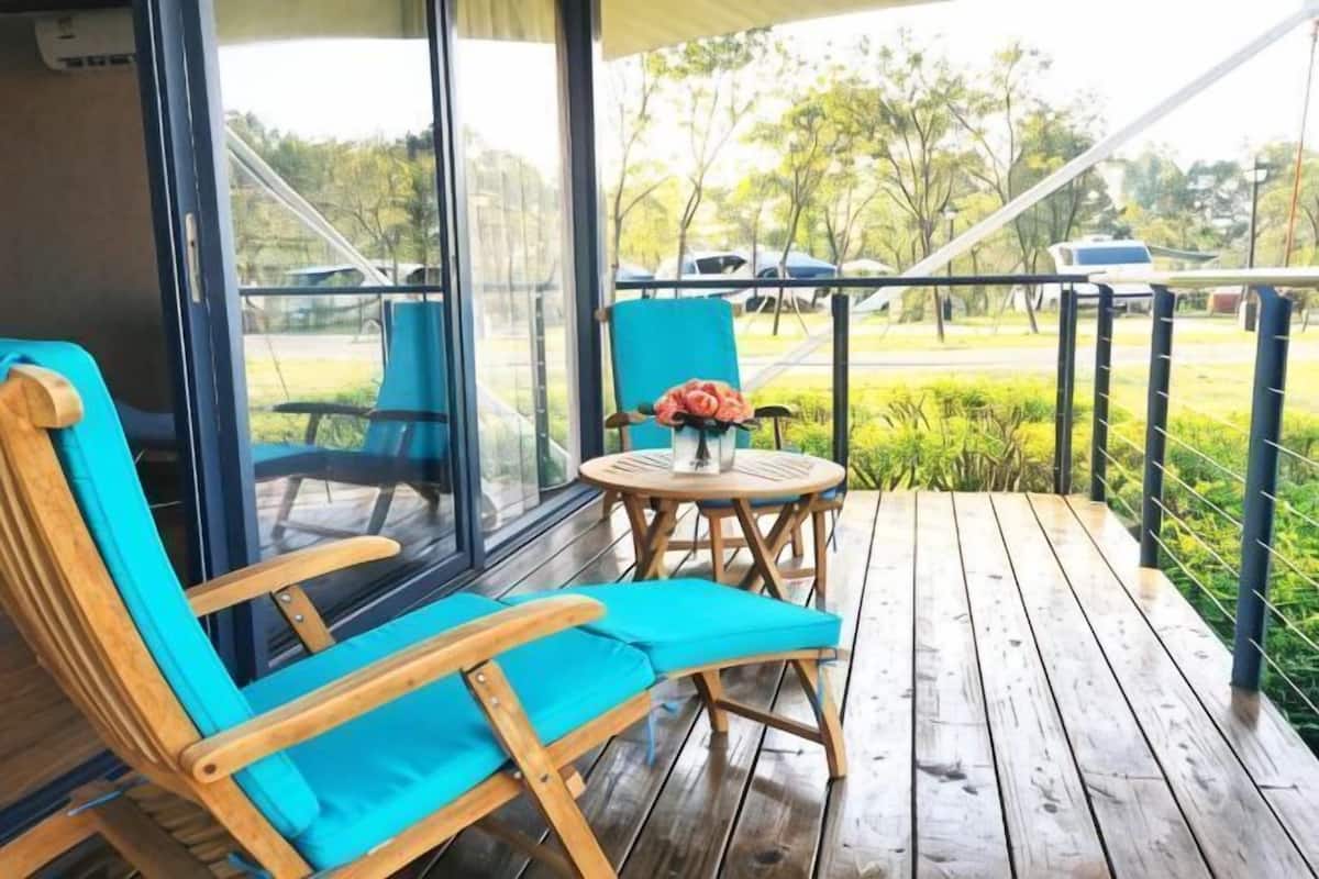 Una terraza de madera con una silla azul y una pequeña mesa con un florero.