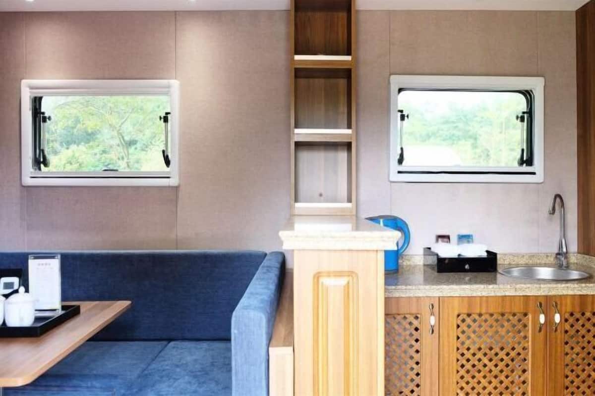 Una kitchenette compacta con dos ventanas, un lavamanos y una zona de estar con una mesa y un sofá azul.