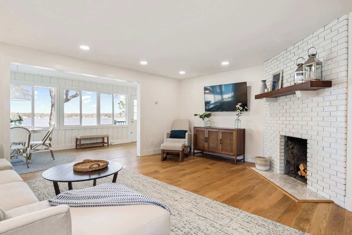 Un salon spacieux avec une cheminée en briques blanches, une grande fenêtre et un coin salon confortable.