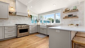 Een moderne keuken met witte kasten, een roestvrijstalen oven en een groot kookeiland met barkrukken.