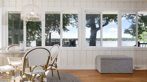 Een kamer met een groot raam, een ronde tafel met stoelen, een witte bank en een hanglamp.