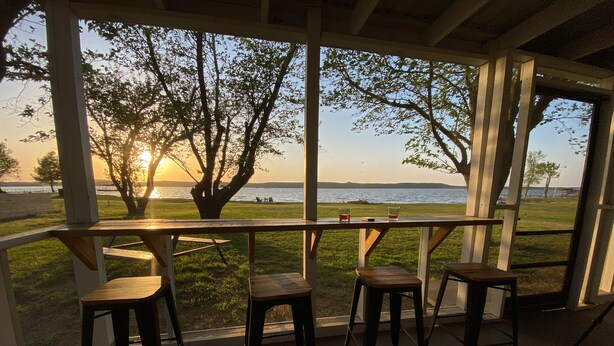 Un espacio de estar techado al aire libre con vistas a la puesta de sol sobre el agua.