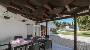 Eine Terrasse im Freien mit überdachter Essgegend, Korbmöbeln und Blick auf den Garten.