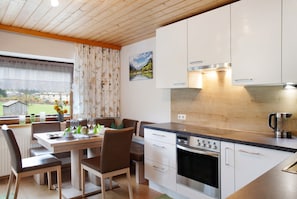 Une cuisine moderne avec des meubles blancs, un four encastré et un coin repas comprenant une table et des chaises.