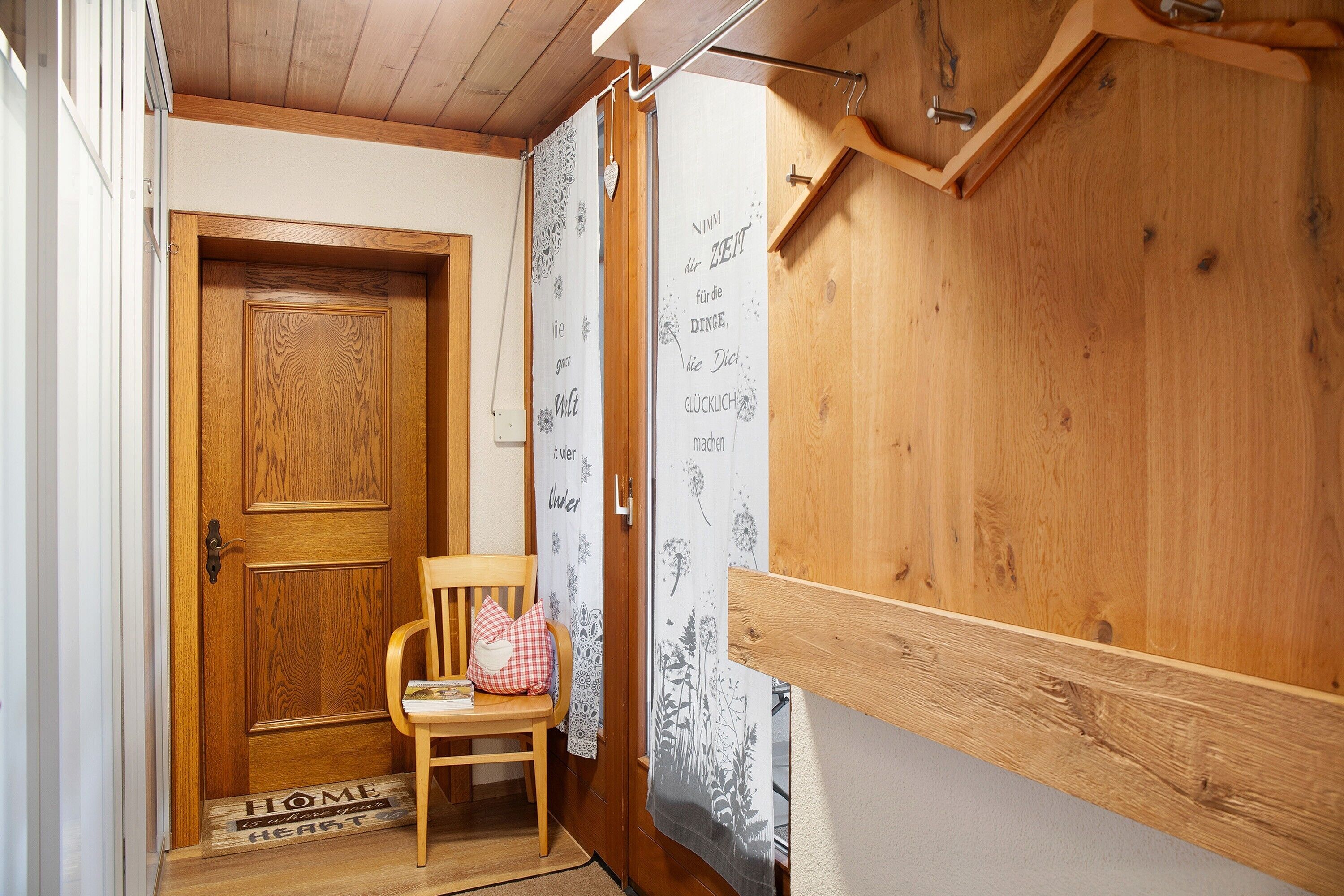 A wooden door, a chair, a doormat, and a wooden wall with a curtain.
