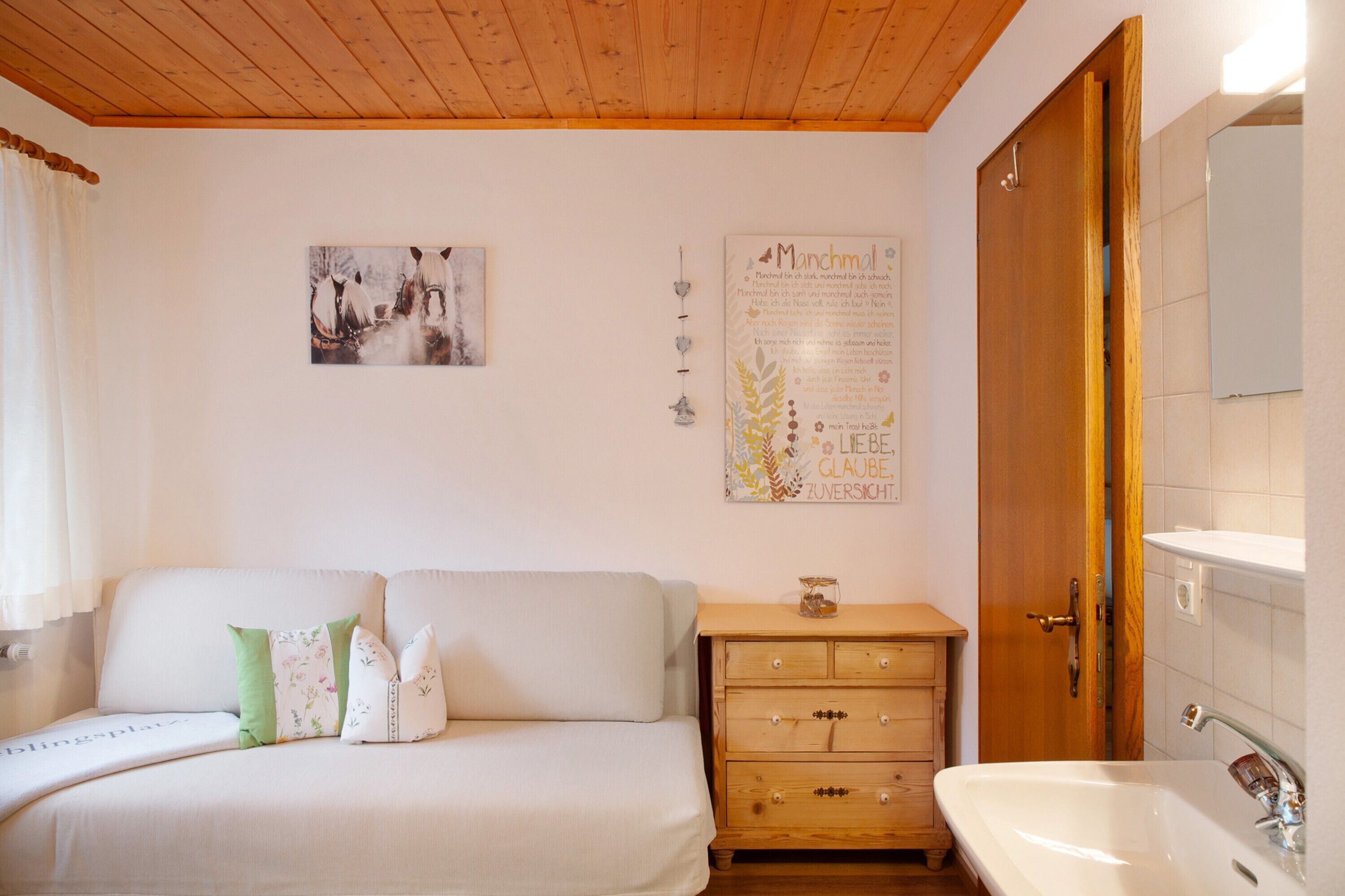 Una camera da letto con soffitto in legno, un letto con cuscini, una cassettiera, uno specchio e un quadro appeso al muro.