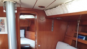 Une petite cabine au décor intérieur en bois, avec un petit lit, un coin salon avec des coussins et une table.